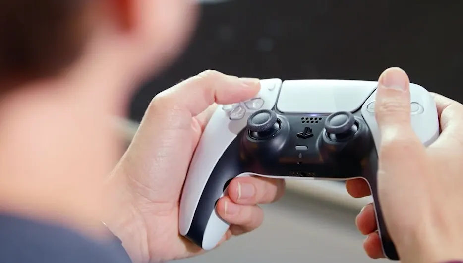 Ein PS5-Controller liegt in zwei Händen. Davor die verschwommenen Umrisse des Spielers.
