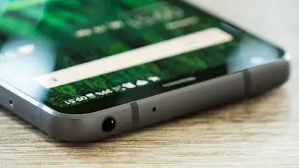 Nahaufnahme eines grauen Smartphones auf einem Holztisch, das Display zeigt die Uhrzeit 09:51.