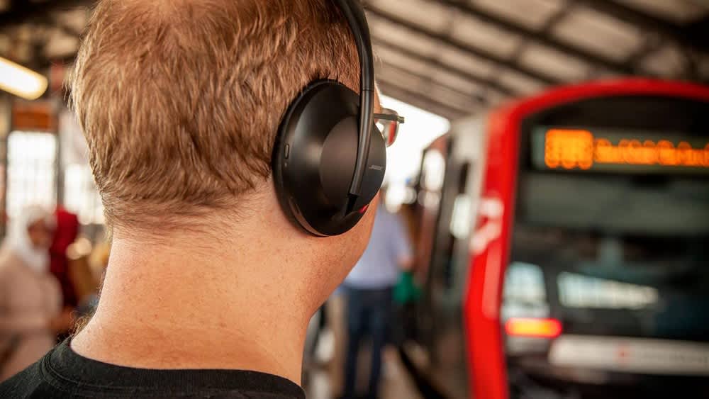 Ein Mann mit den Bose Headphones 700 steht am Bahnhof.