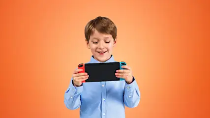 Ein lächelnder Junge hält ein Handheld in der Hand, dass an den Seiten rot und blau ist. Der Hintergrund des Bildes ist orange.
