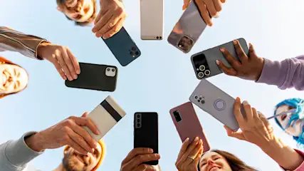 Eine Gruppe hält Handys im Kreis vor einem hellblauen Himmel. Gesichter sind am Rand des Kreises sichtbar.