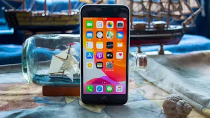 Ein Smartphone mit App-Symbolen steht vor einem Schiffsmodell in einer Flasche und einem anderen Schiffsmodell.