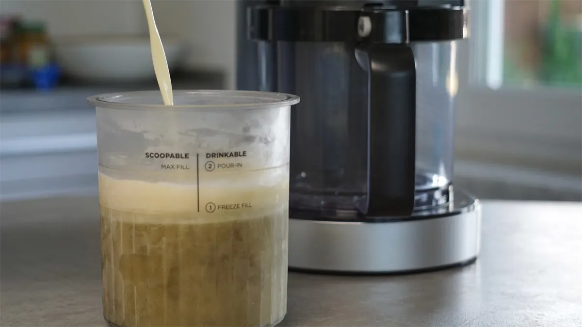 Pflanzenmilch wird in einen Behälter der Ninja Creami Deluxe gegossen.