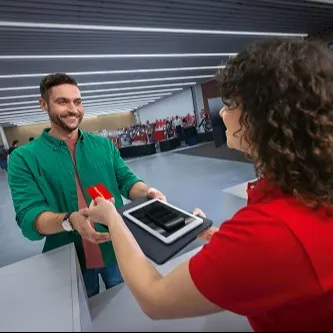 Ein Mann in grüner Jacke tauscht sein Tablet gegen eine rote Karte, welche er von einer Frau in rotem Hemd entgegennimmt.