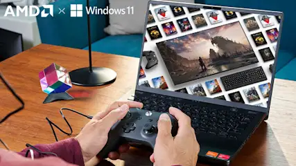 Auf einem Tisch steht ein Laptop, der ein Gaming-Interface anzeigt. Hände halten einen Controller. Logos von AMD und Windows 11 sind sichtbar.