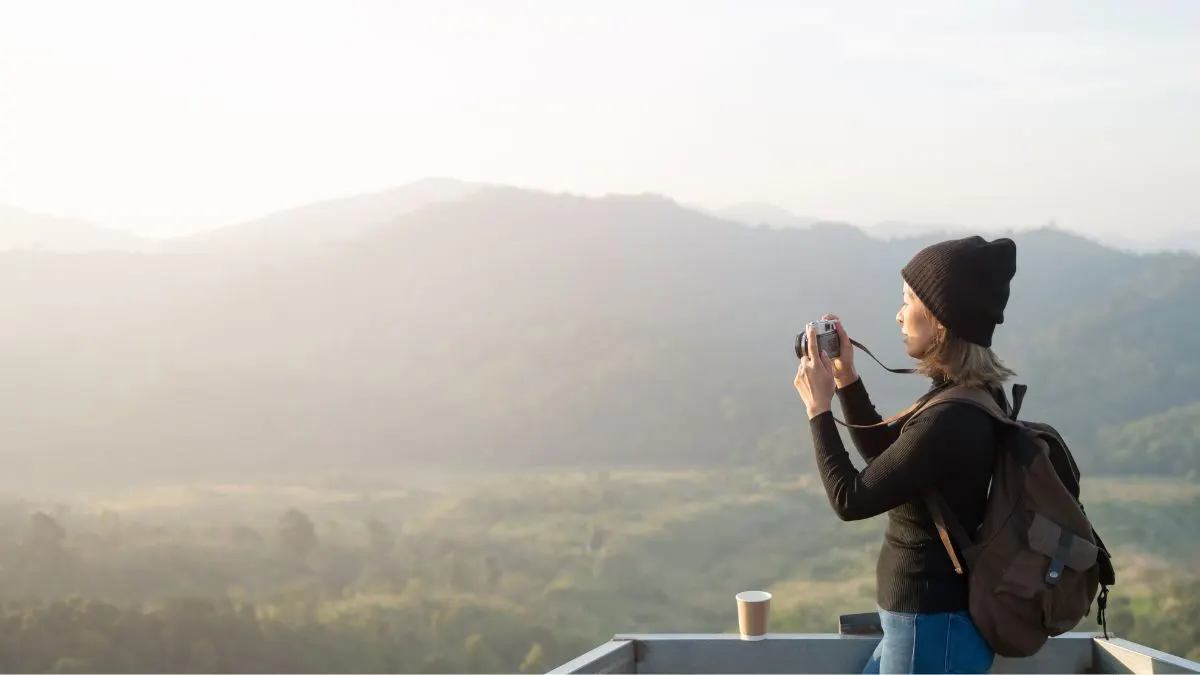 Eine Frau mit Rucksack fotografiert mit ihrer Kompaktkamera das Panorama in den Bergen.