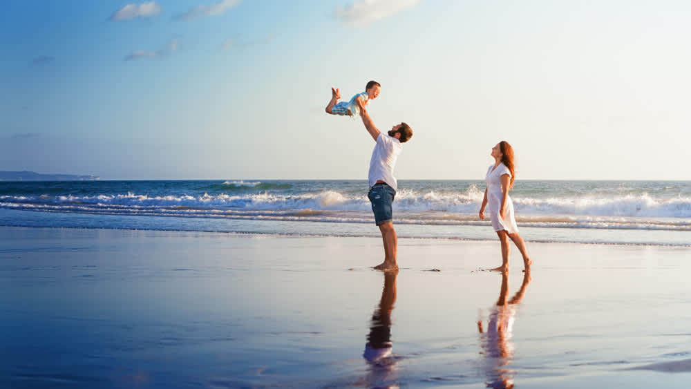 Eine Familie steht am Strand und der Vater hebt das Kind in die Luft.