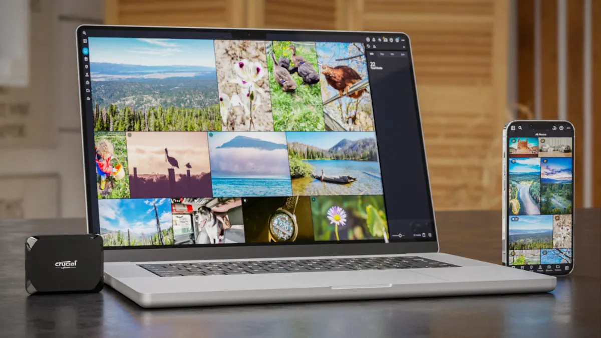 Laptop und Smartphone zeigen Fotoalben neben einer schwarzen Crucial-SSD auf einem Tisch.