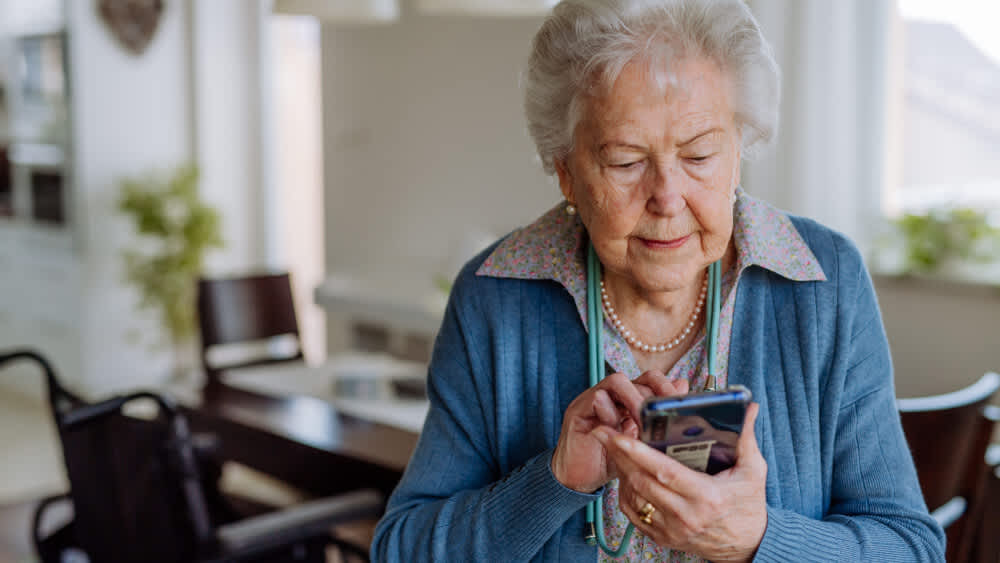 Eine ältere Dame bedient ein Smartphone, dass sie in ihren Händen hält.