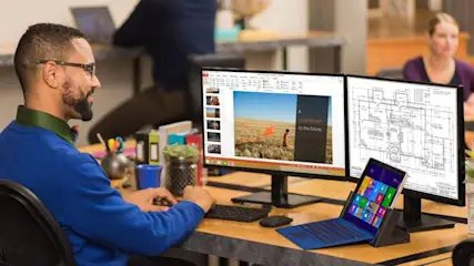Mann in einem Büro an drei Bildschirmen