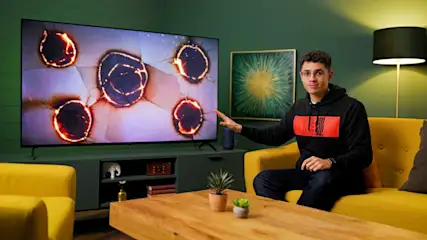 TURN ON Moderator Ilias zeigt auf einen OLED-TV mit simuliertem Einbrenneffekt.