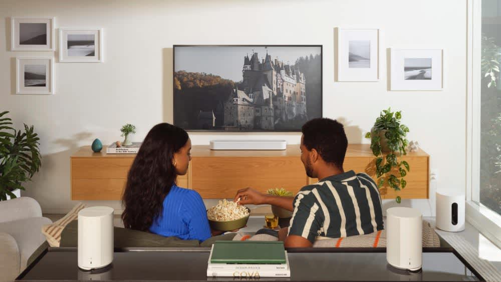 Ein Paar schaut TV mit zwei Sonos Era 100, der Sonos Beam (Gen 2) und dem Sub Mini.