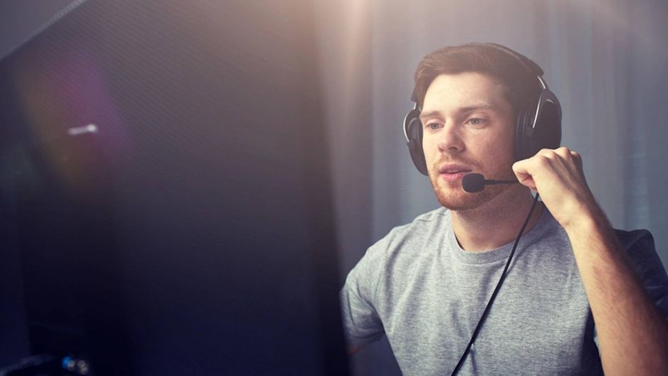 Mann sitzt am Bildschirm und hat ein schwarzes Headset auf