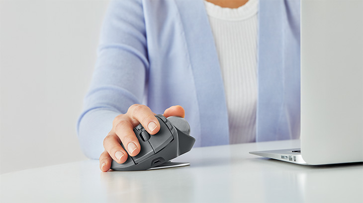 Eine Hand bedient eine ergonomische vertikale Maus auf einem Schreibtisch neben einem Laptop und zeigt komfortables Arbeiten am Computer.