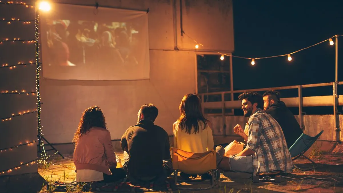 Freunde sitzen auf einem Balkon und schauen einen Film auf einer Leinwand.