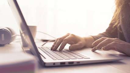 Eine Frau sitzt an einem Schreibtisch und tippt auf einem Laptop.