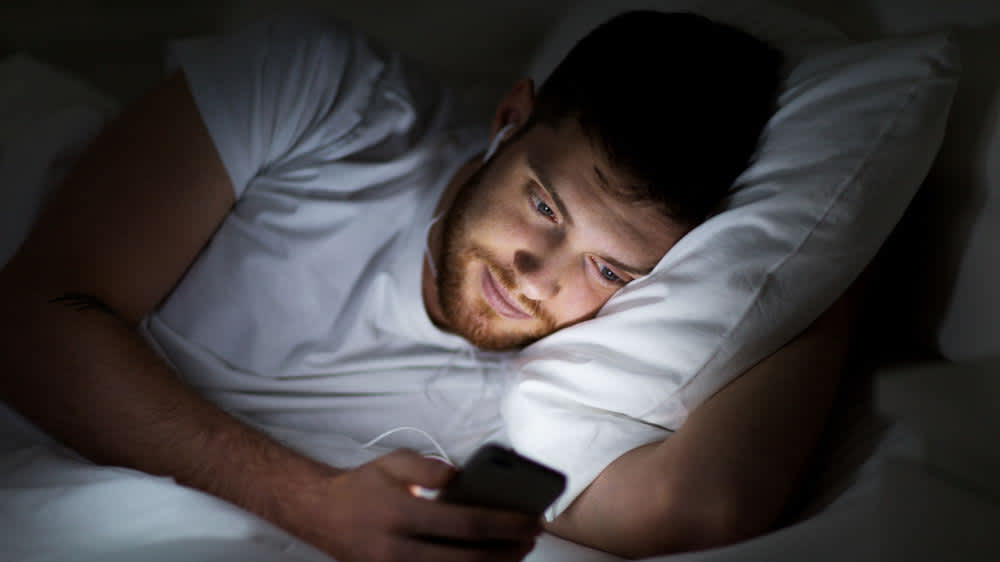 Ein Mann liegt im Bett und schaut auf sein Smartphone.