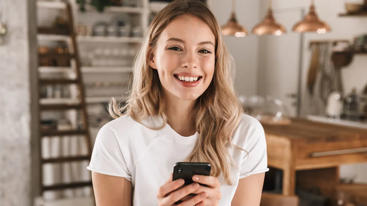 Eine blonde Frau hält ein Smartphone in der Hand und lächelt.