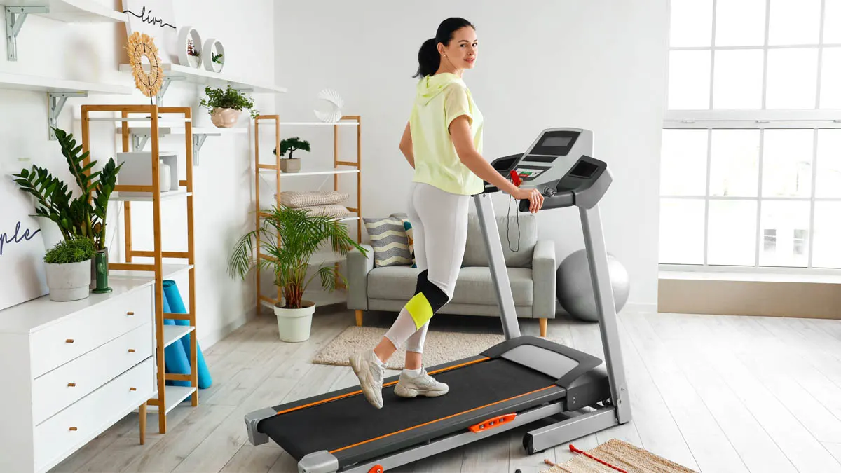 Frau auf einem Laufband in einem hellen Raum mit Regalen, Sofa und Pflanzen.