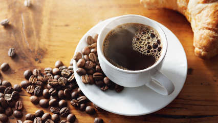 Kaffeetasse von oben mit Kaffee drin und vielen Bohnen daneben am Tisch