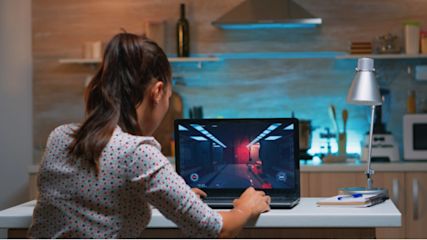 Eine Frau sitzt am Laptop und spielt ein PC-Spiel.