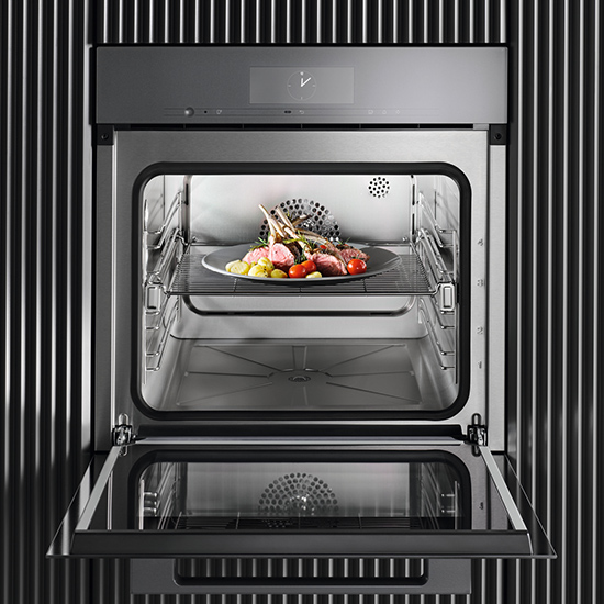 Ein geöffneter, grauer Ofen mit einem Teller Speisen auf einem Rost. Die Speisen bestehen aus Fleisch und Gemüse. Die Ofentür ist geöffnet.