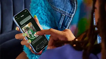 Eine Person hält ein Smartphone mit einer Chat-App in der Hand. Der Chat zeigt ein Foto von drei Hunden im Freien.