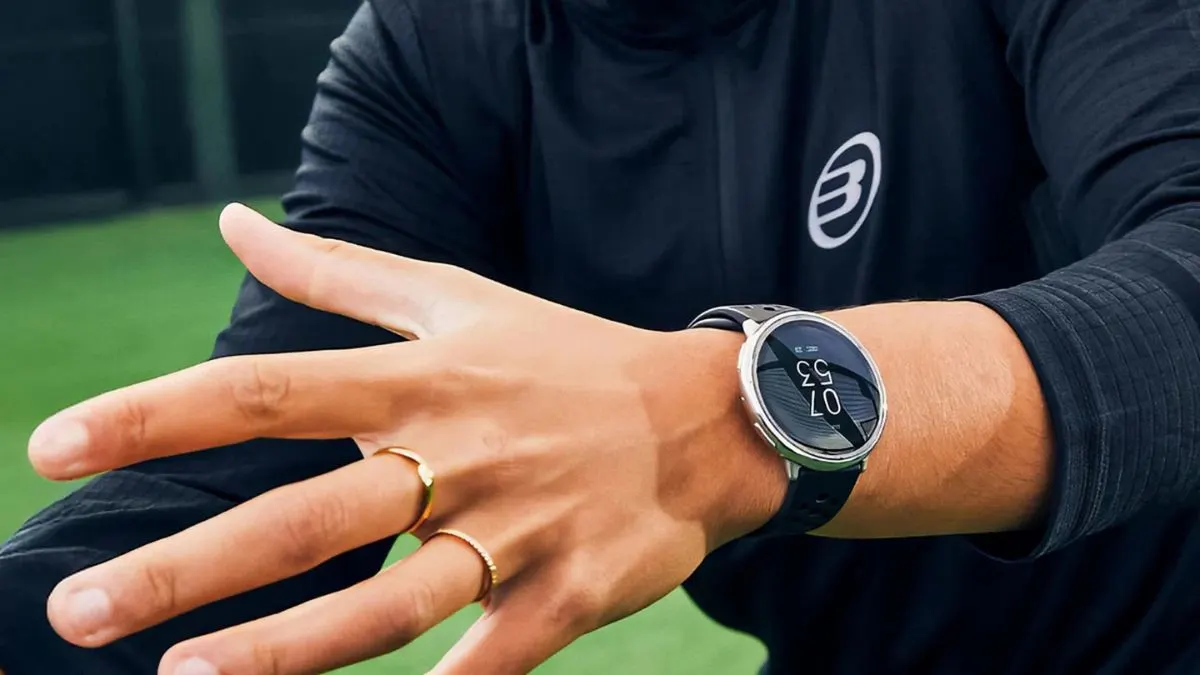 Eine Person trägt ein schwarzes Langarmshirt, zwei goldene Ringe und eine silberne Smartwatch am Handgelenk.