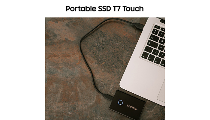 Ein Laptop mit schwarzer Tastatur ist mit einer externen schwarzen Samsung-Festplatte verbunden, die auf einer braunen Oberfläche liegt.