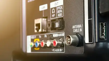Nahaufnahme der Rückseite eines Fernsehers mit verschiedenen Anschlüssen: LAN, Audio, Antenne/Kabel, USB und PC-Audio in Grün, Blau und Rot.