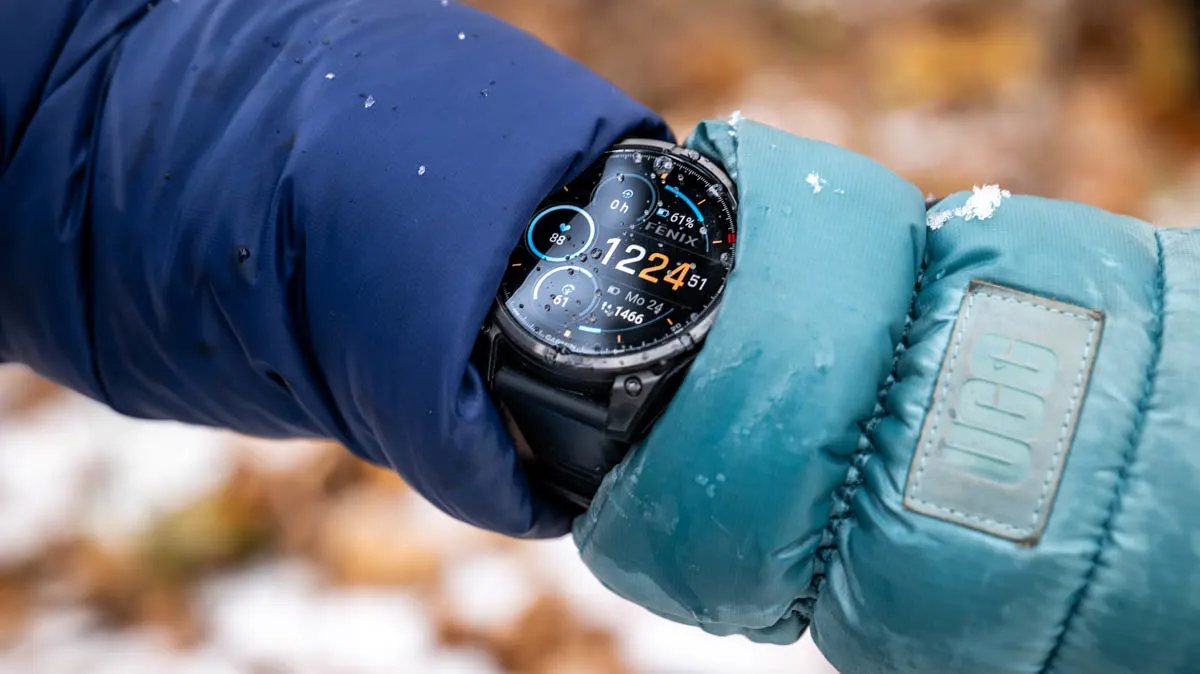 Die Garmin Fenix 8 Pro guckt an Franzis Arm zwischen Winterjacke und Handschuh hervor, auf dem Display ein paar Tropfen geschmolzener Schnee.