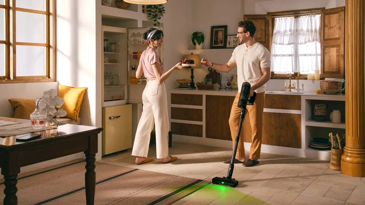 Ein Mann saugt mit dem Roborock H60 Hub Ultra die Küche, während eine Frau ihm etwas zu essen reicht.
