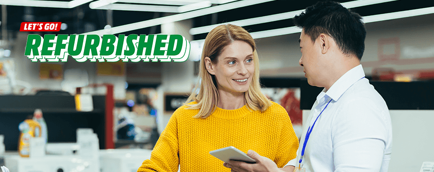 Eine Frau im gelben Pullover hält ein Tablet und spricht mit einem Mann im weißen Hemd in einem Geschäft.