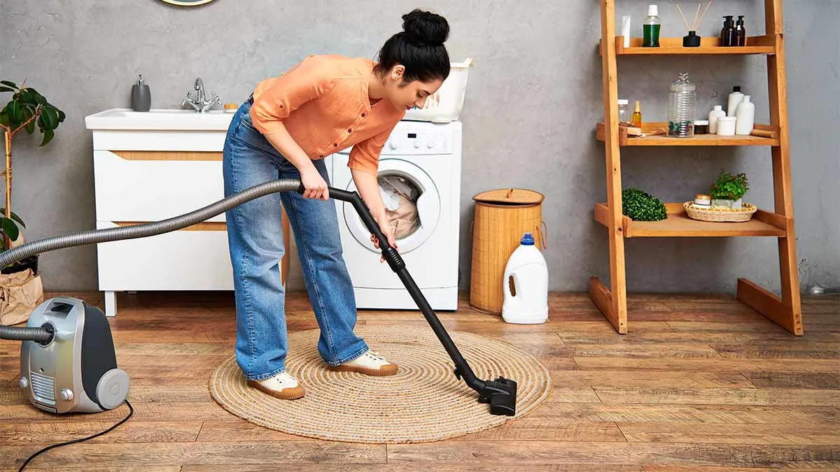 Frau saugt einen runden Teppich auf einem Holzboden. Im Hintergrund steht eine Waschmaschine.