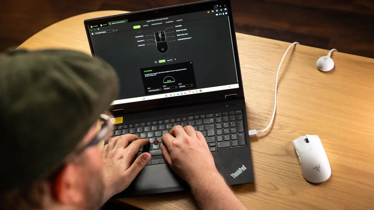 Andreas tippt auf einem ThinkPad. Auf dem Bildschirm ist die Software zur Maus Razer Viper V4 Pro zu sehen, die rechts neben dem Laptop liegt.