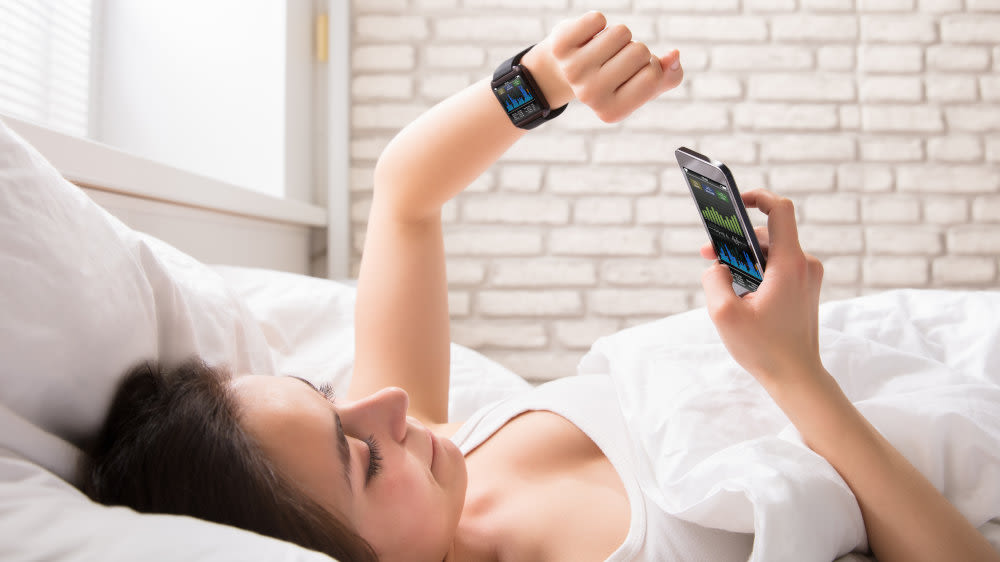 Eine mit einer Smartwatch am Arm liegt im Bett.