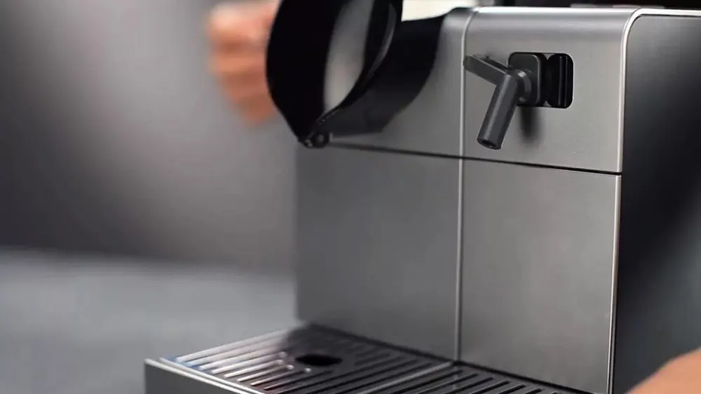 Eine Kaffeemaschine aus Metall mit einem Hebel und einer Abtropfschale steht auf einer grauen Oberfläche.