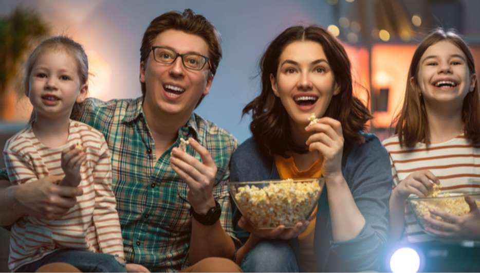 Frontalaufnahme einer Famile, die vor dem Fernseher sitzt und Popcorn isst