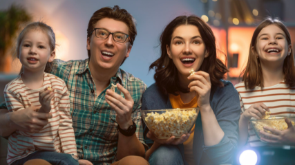 Frontalaufnahme einer Famile, die vor dem Fernseher sitzt und Popcorn isst