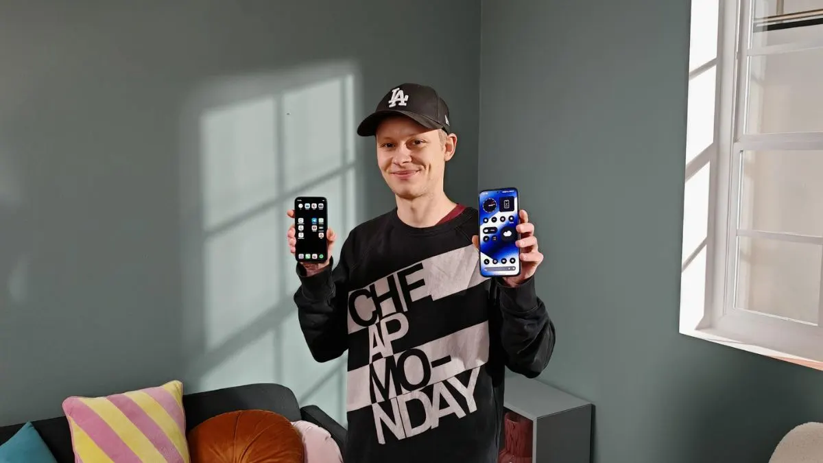 Alex steht in einem Wohnzimmer und hält ein iPhone 12 Mini und ein Nothing Phone (2a) Plus in die Kamera.