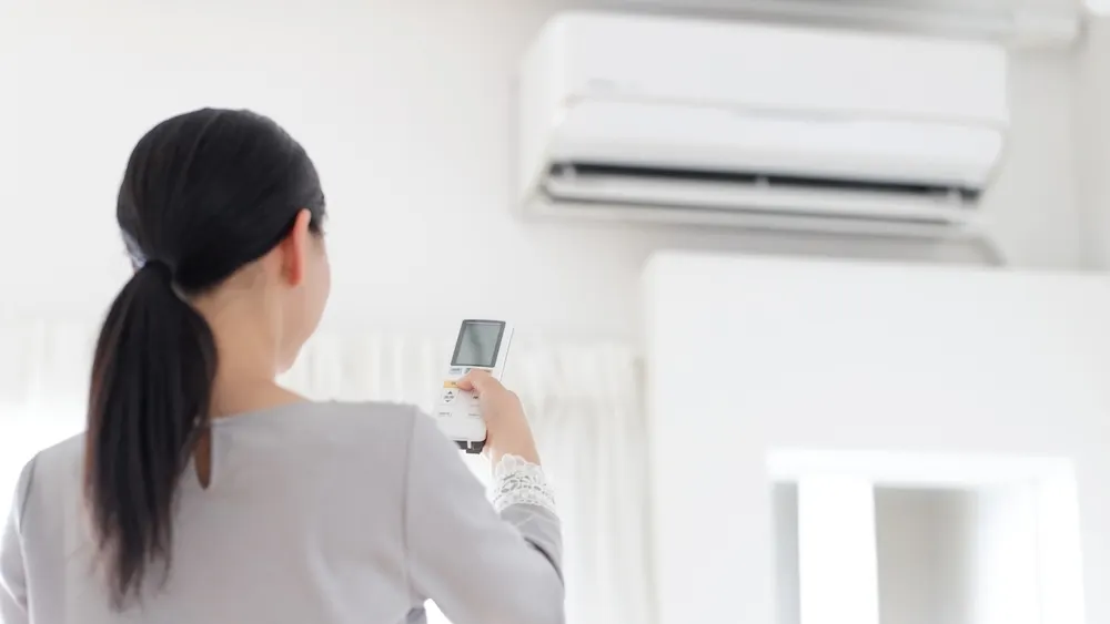 Eine Frau richtet eine Fernbedienung auf eine Klimaanlage.