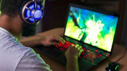 Mann sitzt im Dunkeln vor einem Gaming-Laptop und zockt.