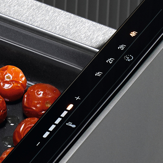 Nahaufnahme von Tomaten auf einem Backblech neben einem Bedienfeld mit Timer- und Temperatureinstellungen.