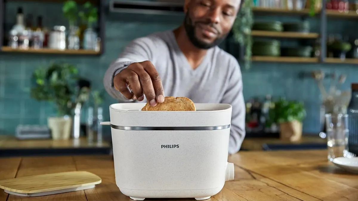 Ein Mann steht in einer Küche und nimmt eine Scheibe Toastbrot aus dem Toaster Philips HD2640/10.