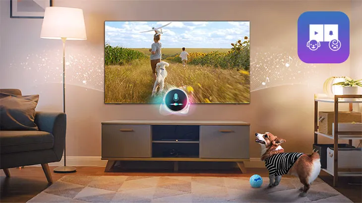 Das Bild zeigt ein gemütliches Wohnzimmer mit einem großen Fernseher, auf dem eine Szene mit zwei Personen und einem Hund in einem sonnigen Feld zu sehen ist. Die Personen laufen fröhlich durch die Blumenwiese, während der Hund mit ihnen spielt. Vor dem Fernseher steht ein eleganter TV-Ständer, auf dem ein Sprachassistent mit einem leuchtenden Symbol zu sehen ist. Im Vordergrund befindet sich ein Corgi-Hund, der mit einem blauen Ball spielt. Eine Lampe sorgt für warmes Licht und eine einladende Atmosphäre im Raum. In der oberen rechten Ecke des Bildes ist ein Symbol zu sehen, das auf Funktionen für interaktive Medien hinweist.
