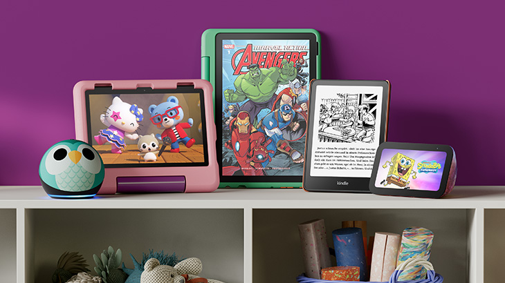 Auf einem Kinderzimmer-Regal stehen verschiedene Amazon-Geräten für Kinder: Echo Dot im Eulen-Design, rosa und grünes Fire-Tablet, Kindle und Echo Show.
