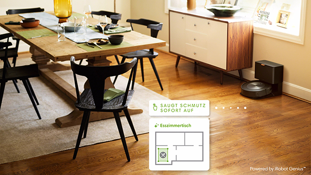 Ein Esszimmer mit Holztisch, Stühlen, Teppich und Sideboard. Ein Roboterstaubsauger steht am Rande eines Holzfußbodens.