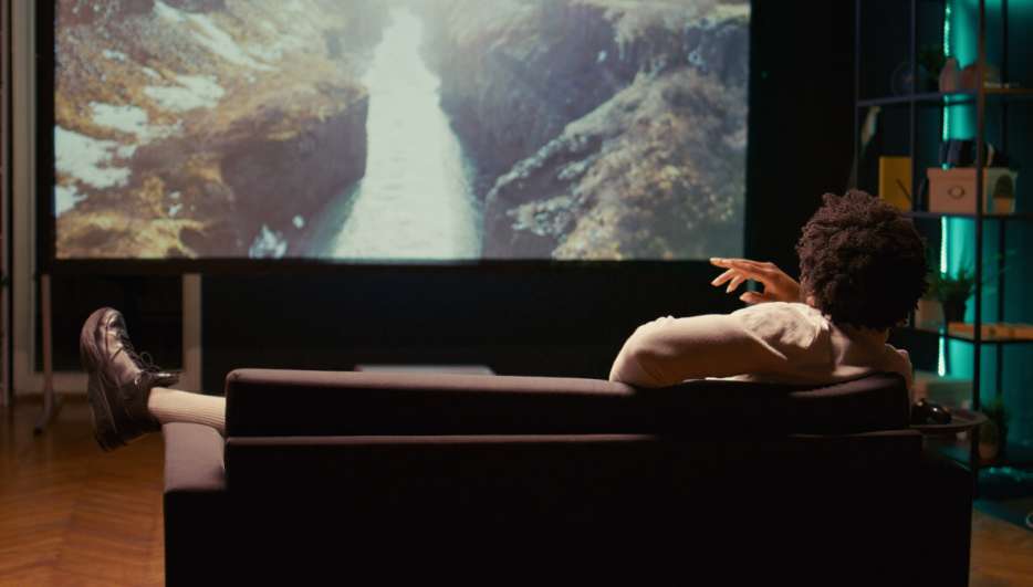 Ein Mann sitzt auf der Couch und schaut einen Film über einen Beamer.
