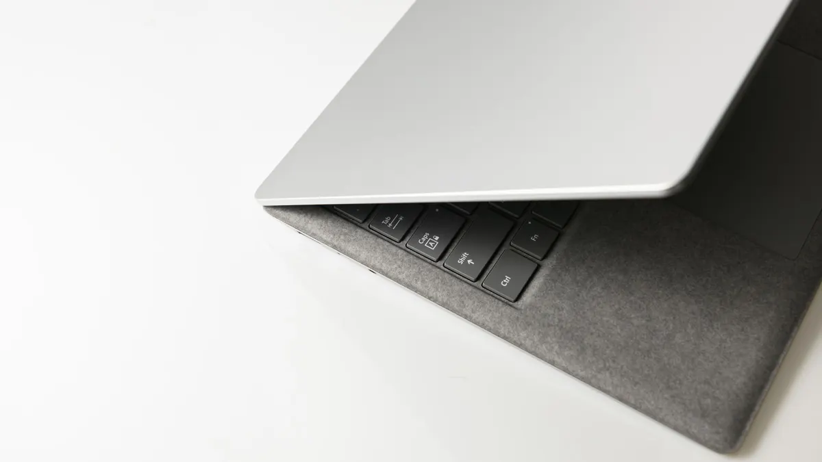Ein Laptop liegt auf einem weißen Tisch, der Deckel ist leicht geöffnet und gibt den Blick auf die schwarze Tastatur frei.