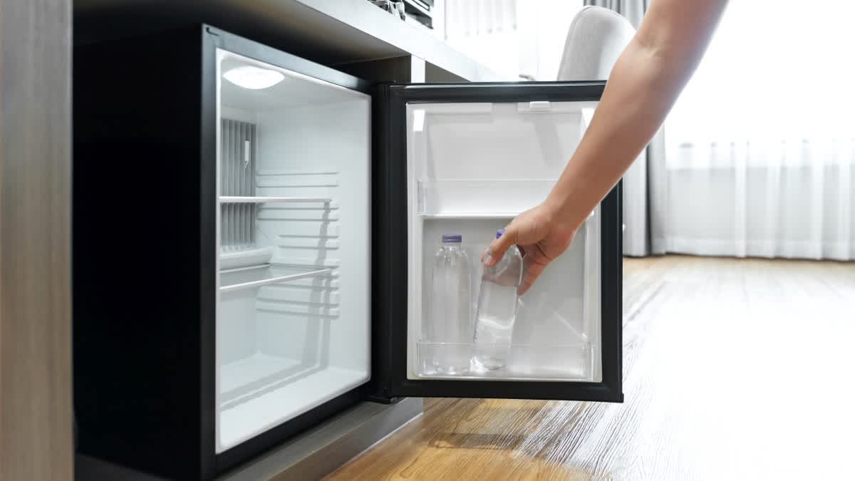 Eine Person nimmt eine Flasche Wasser aus einem Mini-Kühlschrank heraus.